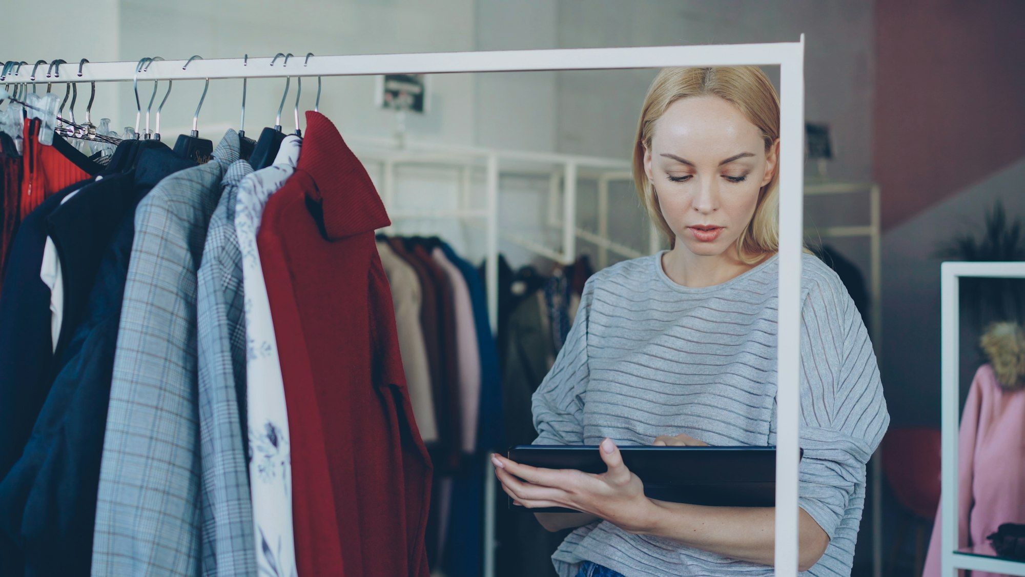 A boutique owner checking garments on the clothing racks while updating stock on a tablet
