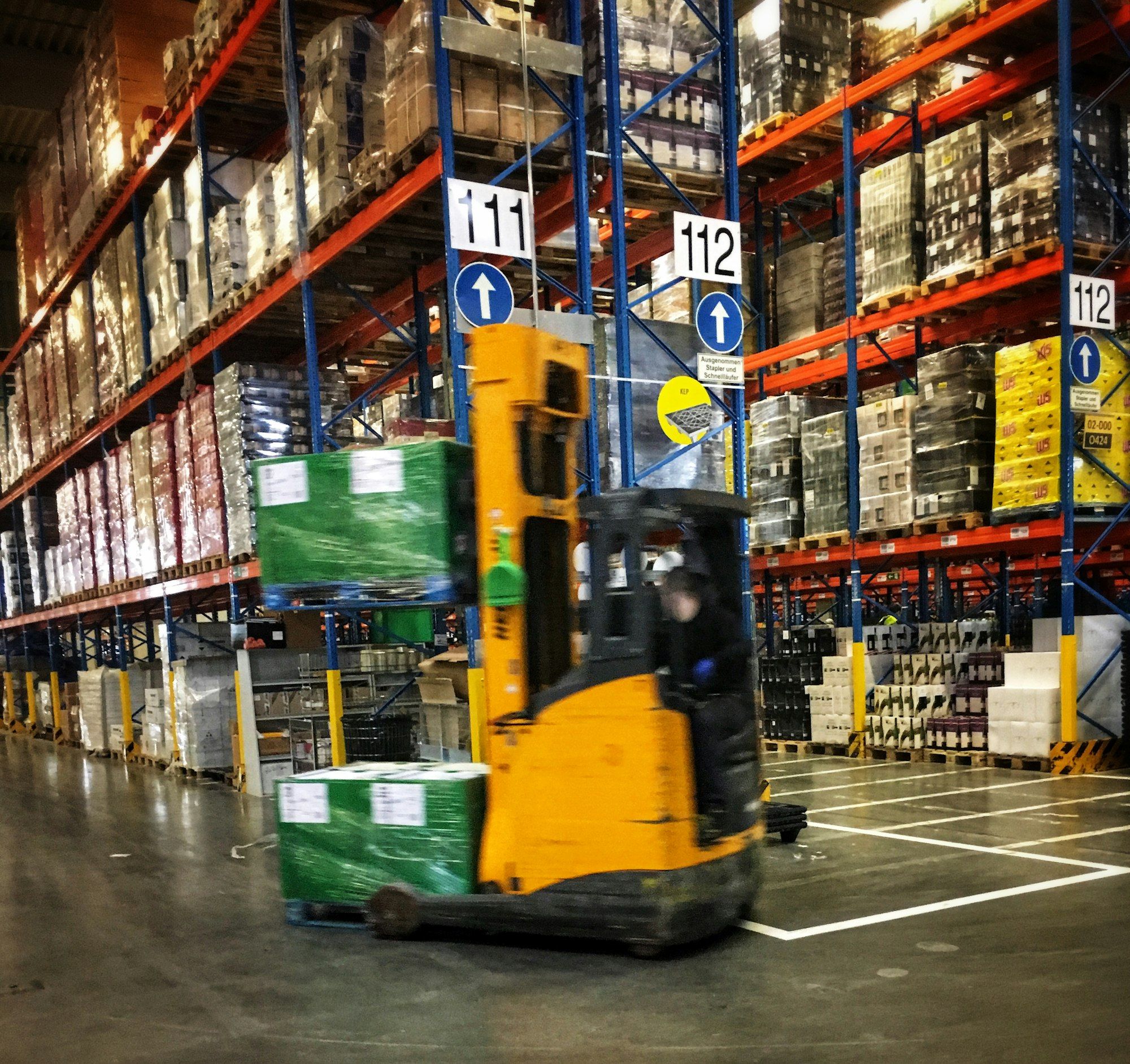 A forklift driving down an aisle of tall pallet racking in a distribution warehouse