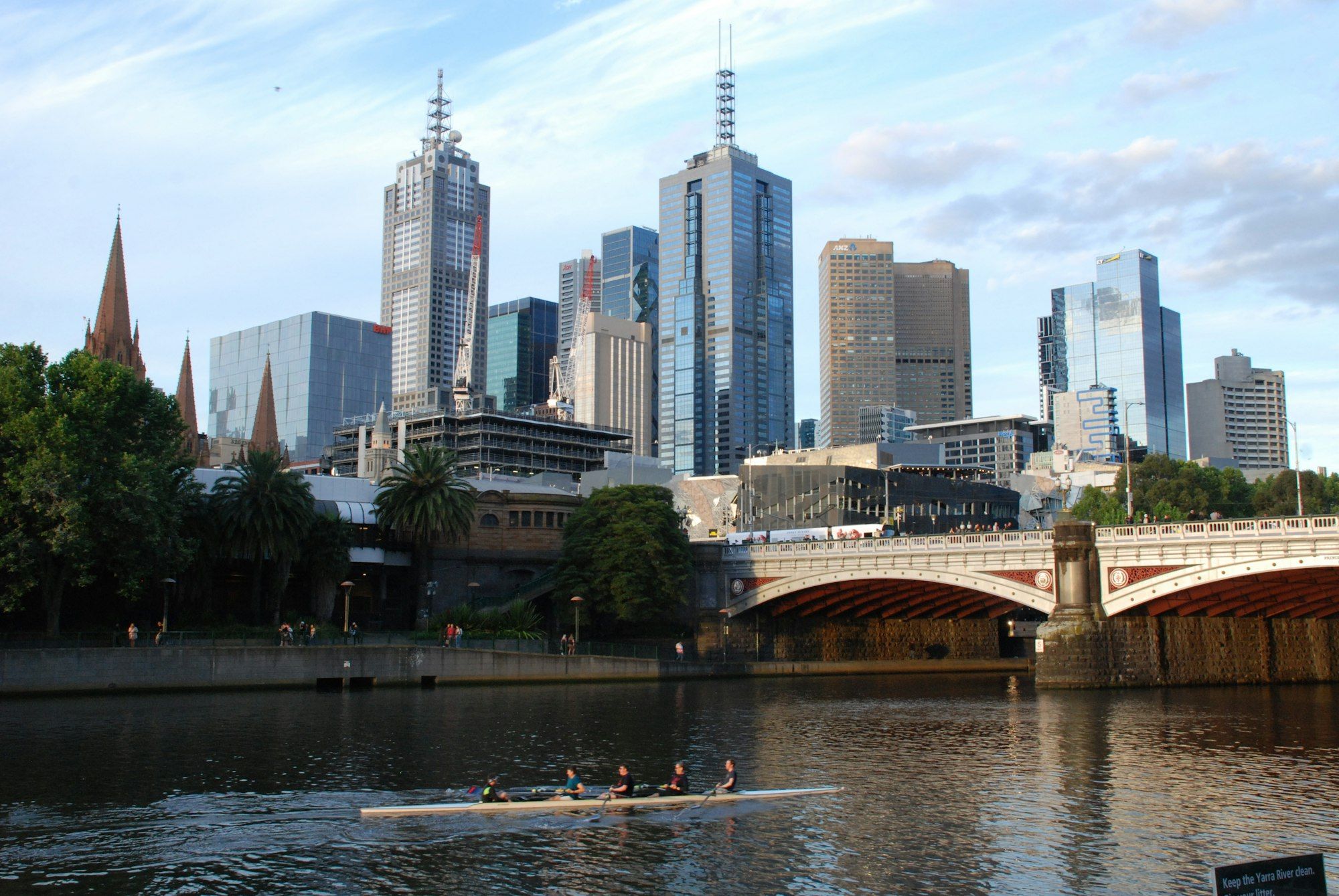 Rowers on the Yarra River beneath a bridge with the Melbourne city skyline behind
