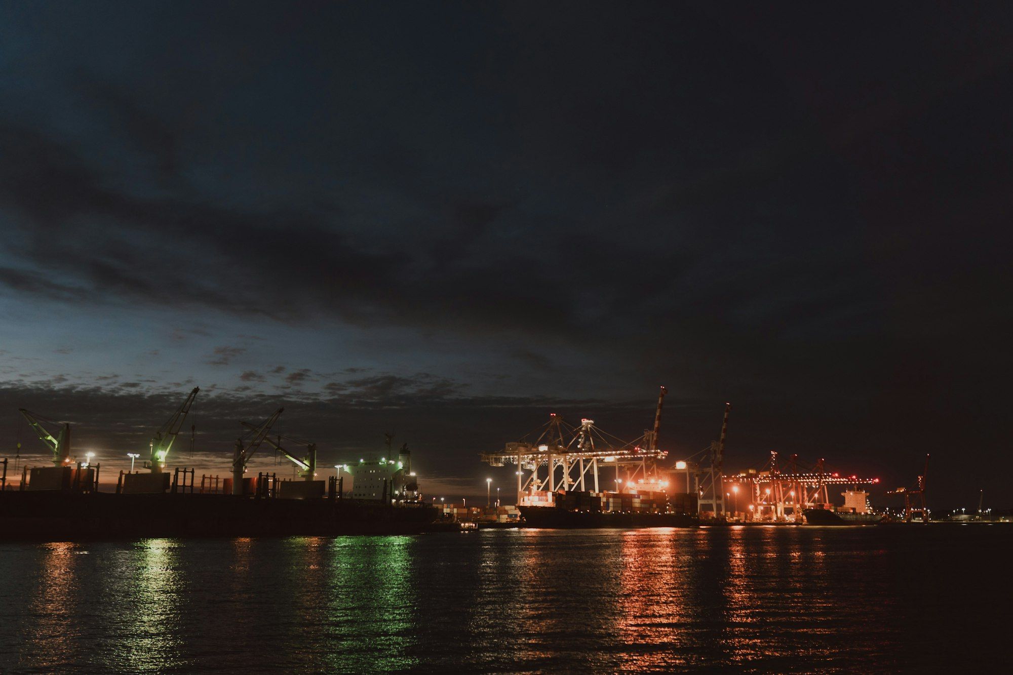 Container cranes and cargo ship lit up at dusk at Fremantle port, Western Australia